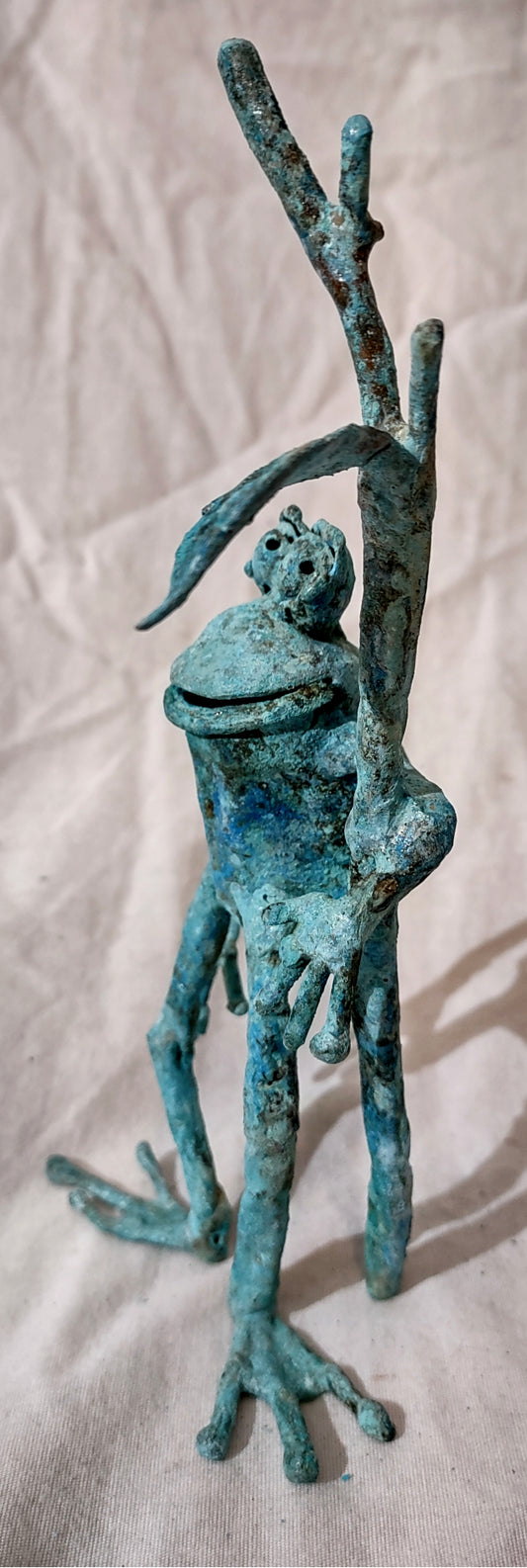 Copper froglette figurine. Standing, holding onto a branch.